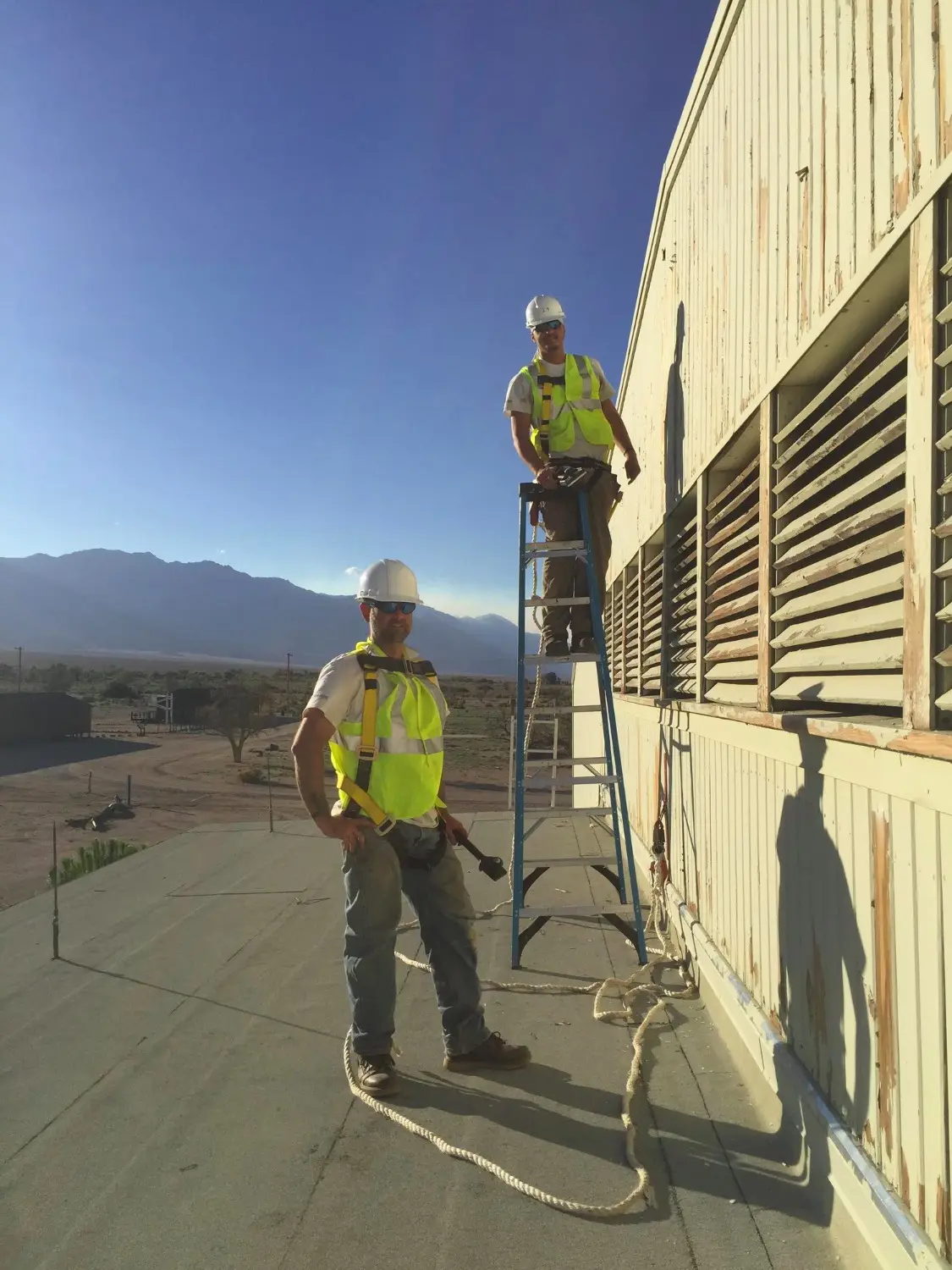 Two painters in safety vests prepping the louvered wall of a commercial building